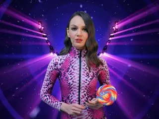 PrincessWaltrude poses in a long-sleeved purple and pink patterned top, looking directly at the camera with her dark hair down.