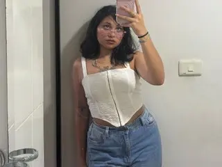 Young woman in a white corset top and blue denim jeans taking a mirror selfie in a modern room.