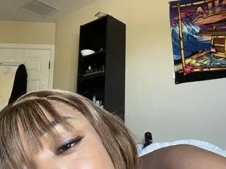 ProductivePussy looks into the camera with her brown hair and eyes, showing her face and bare shoulders against a plain wall.