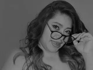 Pukkared poses with a close-up headshot, wearing black glasses and showing her long, wavy hair in a black and white photo.