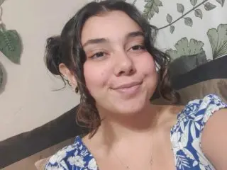 PunkPupp smiles while looking at the camera, showing her dark wavy hair and wearing a blue and white floral print top.