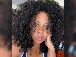 QueenJhonson poses with her dark curly hair framing her face, showing her bare shoulders and neck in a close-up shot.