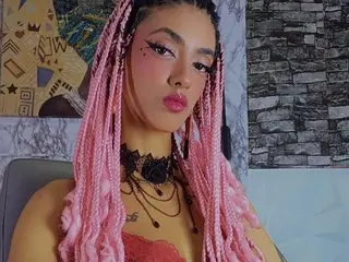Queen_Cuarxooo poses with long pink braids, wearing a black lace choker and a red lace bra against a textured wall background.