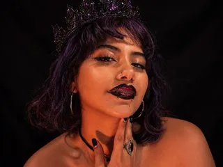 RAVENTEEN wears a dark crown and black lipstick while posing against a black background.