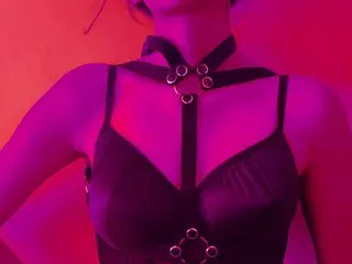 ROOH28B poses in a black halter-style top with silver ring details against a warm, red-lit background.