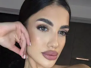 Raisa_Kali poses close-up, showing her face, dark hair, and thick eyebrows with a soft glow on her skin.