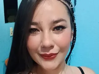 Rapunsel_hl smiles for a close-up selfie, showing her long dark hair and makeup against a bright blue wall.