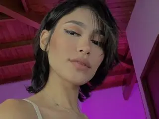 Ravemiisato poses close-up with her dark hair framing her face, looking directly at the camera against a purple-lit background.