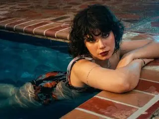 Raven_Morningstar with dark hair poses in a swimming pool wearing a patterned swimsuit.
