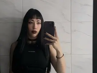 Goth girl with long black hair and dark makeup wearing a black tank top taking a moody mirror selfie.