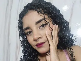 RayliCurly with curly dark hair posing with her hand on her face against a marble wall.