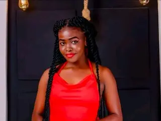 Smiling Black woman in a red satin halter top with long braids posing against a dark background.
