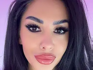 RileyNox looks directly into the camera with long eyelashes and dark hair framing her face.