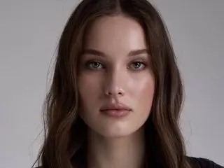 RiwaEnergy poses with a direct gaze, showing her face and long brown hair against a plain grey background.