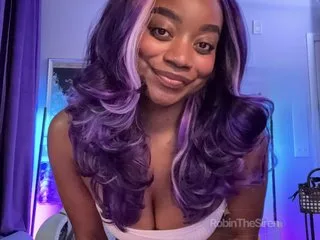 RobinTheSiren smiles at the camera with long purple hair while wearing a white tank top.