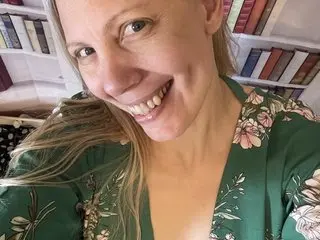 Smiling woman in a green floral blouse relaxing in a cozy home library setting.