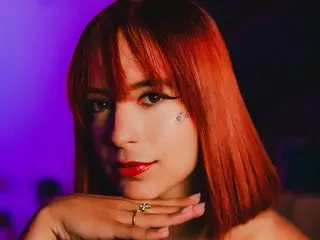 RomaSun poses with her red hair and blunt bangs, looking directly at the camera with red lipstick on.