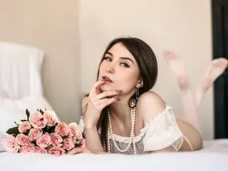 Beautiful young woman in white lace lingerie lying on a bed with a bouquet of pink roses in a romantic mood.