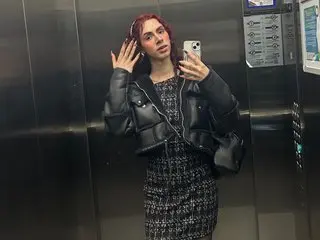 Rosedorry poses for a mirror selfie in a dark patterned dress, holding a phone while showing her red hair and bare shoulders.