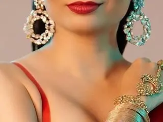 RosyCurvy poses with red lipstick and large gold earrings, wearing a red strap top against a soft background.