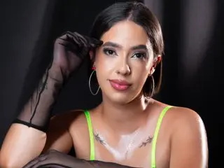 RousMonroe poses in a neon green top and sheer black gloves against a dark background.