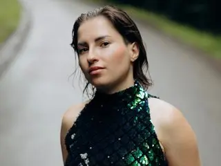Roxiq poses in a dark green sequined halter top, looking directly at the camera with her dark hair pulled back.