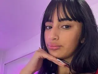 RoxxaneDamiana poses for a close-up selfie with long dark hair and bangs against a purple background.