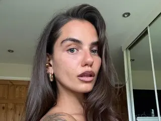 RoxyRoseX looks into the camera with a close-up selfie pose, showing her long brown hair and gold hoop earrings.
