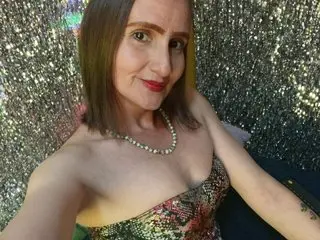 RubiHolmes poses in a strapless floral top, showing her shoulders and chest against a shimmering silver glitter background.