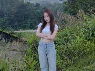 Young woman in white crop top and light blue jeans standing in a lush green meadow during a peaceful day.