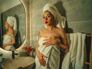 RubyMills poses naked with a white towel wrapped around her chest and head, showing her bare shoulders and cleavage in a bathroom setting.