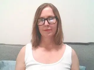 SWEETandNAUGHTY21 wears a white tank top and glasses while looking directly at the camera against a plain wall.