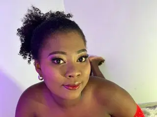 Beautiful Black woman with curly hair and red makeup posing in a red outfit against a soft purple background.