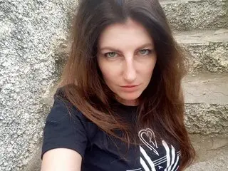 SabrinaDeep looks at the camera with long brown hair, wearing a black t-shirt with a white graphic, posing against a textured stone wall.