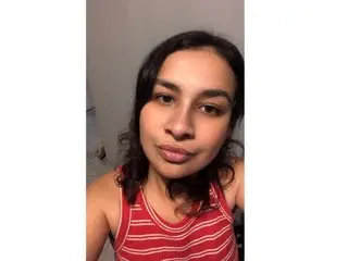SabrinaFlorez poses with a soft smile, showing her dark hair and wearing a red and white striped tank top against a plain wall.