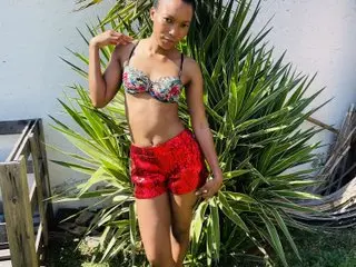 SaggyTitties188 poses outdoors in front of green leaves, wearing a patterned bikini top and red sequined hot pants.