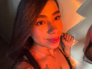 SalomeOwen poses close-up with long dark hair, wearing a black top and a gold necklace against a light-colored background.