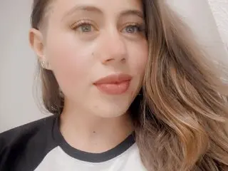 Salomejohn looks at the camera with long brown hair and a neutral expression, wearing a white and black top.