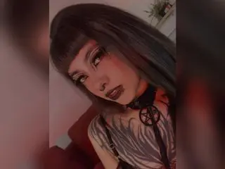 Goth girl with dark bangs and pentagram choker posing in moody red lighting.