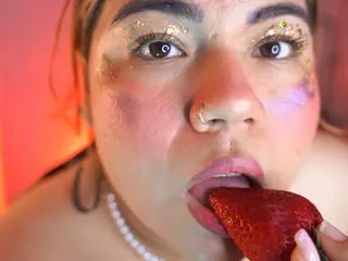 SamantaLovexxx licks a red strawberry with her mouth open, showing her teeth and wet lips in a close-up shot.