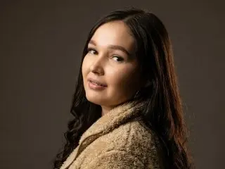 Smiling young woman with long wavy hair wearing a cozy beige fleece jacket in a studio setting.