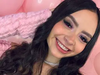 SamiVegga smiles with long dark hair, wearing a light pink knit sweater or top.