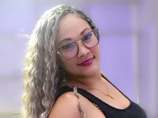 SamiraLennox poses with long, wavy blonde hair and glasses, wearing a black tank top against a soft purple background.