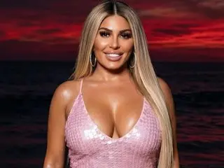Smiling blonde woman in a pink sequin cocktail dress at sunset by the ocean.