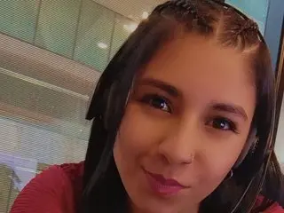 Sammy_kriss looks at the camera with her dark hair styled in small braids, wearing a red top against a soft-focus background.