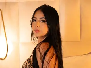 Young woman with long black hair wearing a leopard print top in warm, moody indoor lighting.