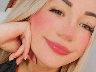 Sara019 smiles close up, showing her face, blonde hair, and pink blush on her cheeks.