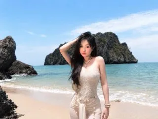 SaraVenis poses on a sunny beach in a white lace bodysuit with her hand in her long dark hair.