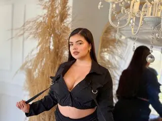 Curvy woman in a black crop top outfit posing elegantly in a bright room with pampas grass decor.