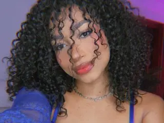 Saraa_Gomez has curly dark hair and wears a blue lace top while looking at the camera.